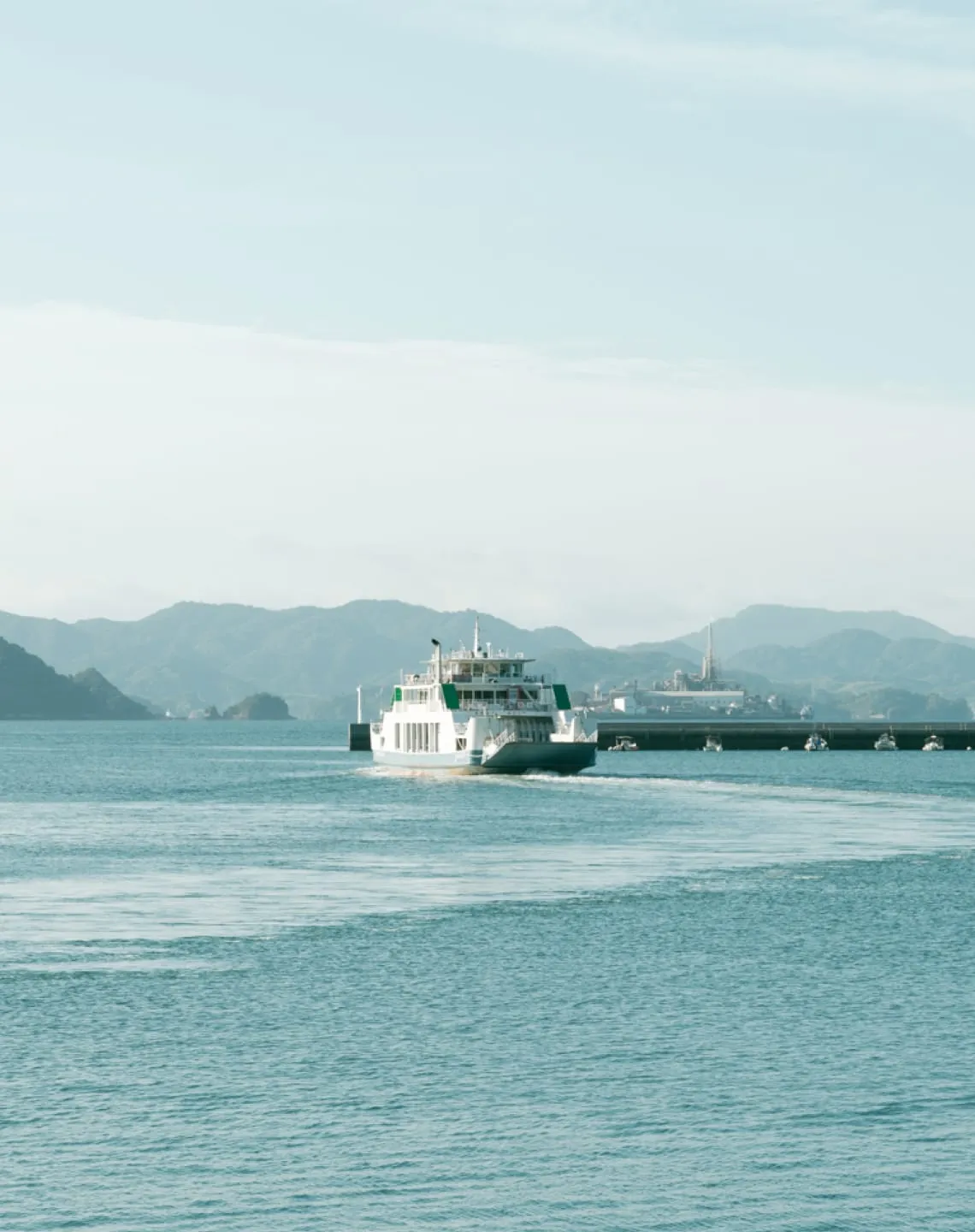 A traditional festival boat carrying lanterns sails across the sea against an industrial backdrop.