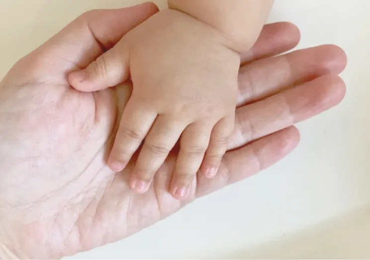 赤ちゃんの小さな手を大人の手が優しく包み込んでいる様子