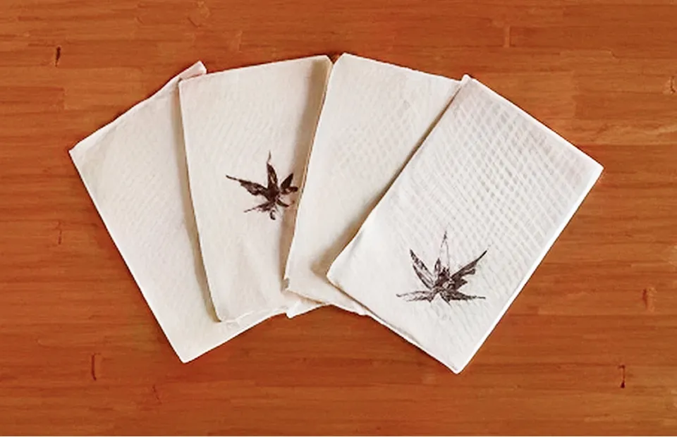 나무 무늬 테이블 위에 부채꼴로 펼쳐진 4장의 하얀 직사각형 화지. 각각의 화지에는 초목 염색 같은 기법으로 식물 잎(단풍 모양)이 갈색으로 중앙에 하나씩 프린트되어 있다. 수제 느낌이 나는 소박하고 섬세한 공예 작품.